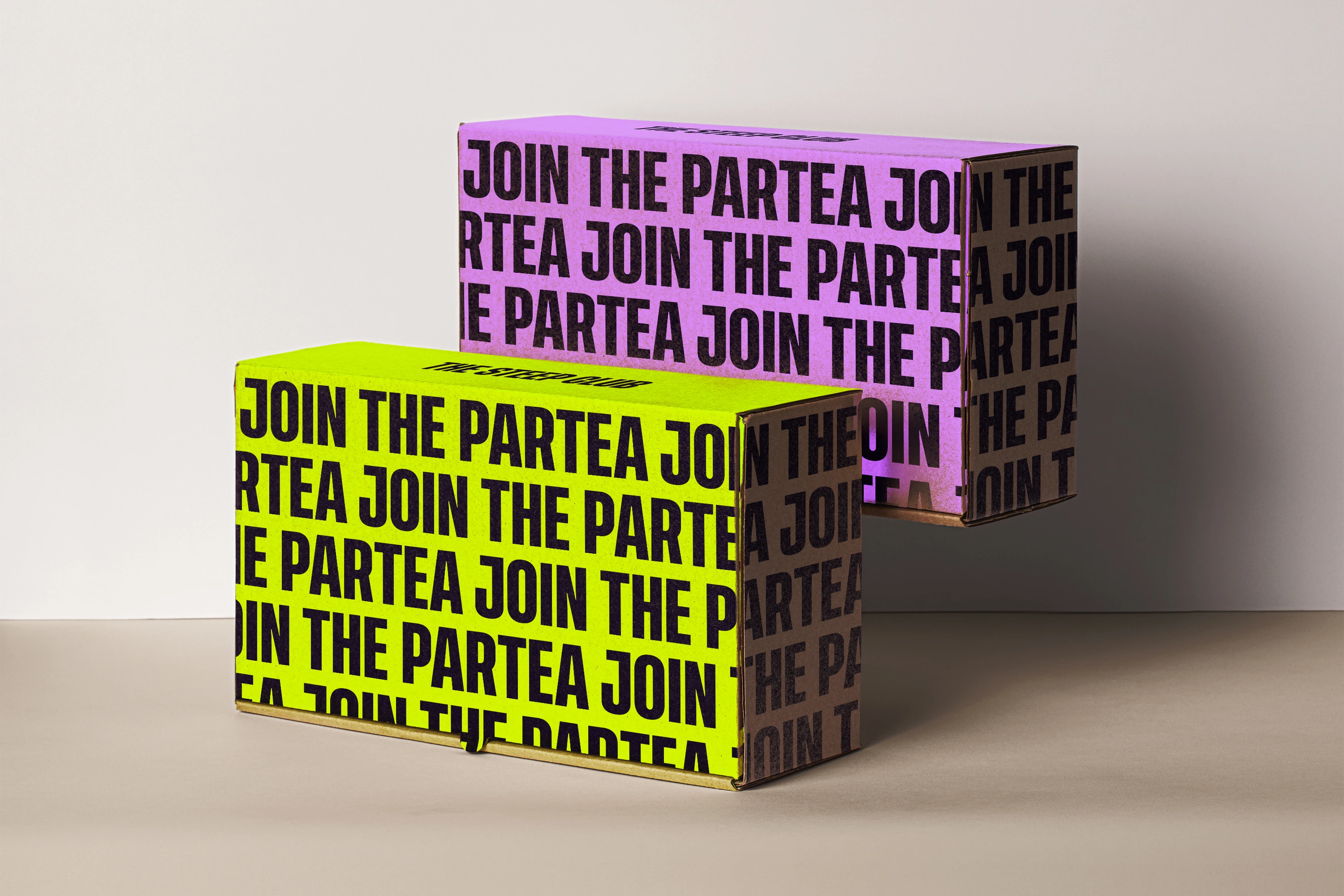 Two Steep Club shipping boxes stacked on a table, one acid yellow and one purple, each covered edge to edge in “Join the Partea” in heavy black capitals